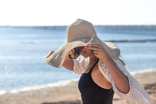 波西米亚穿泳衣的女孩用一顶大帽子遮住脸海上避暑的概念特写年轻斗篷