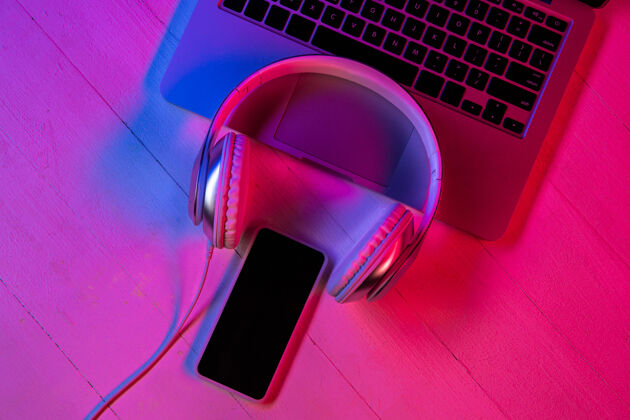 数字紫色霓虹灯和粉色背景的一组小工具的俯视图笔记本电脑键盘 耳机和带黑屏的智能手机广告的复制空间科技 现代 小工具技术小工具移动