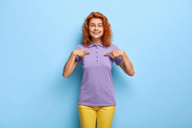 女性化喜气洋洋的红发女人指着t恤的空白处发型服装满意