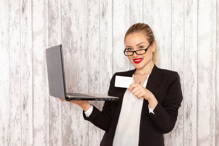 手持正面图：穿着黑色夹克的年轻女商人 用她的笔记本电脑 在浅白的表面上拿着名片女业务员办公室严格