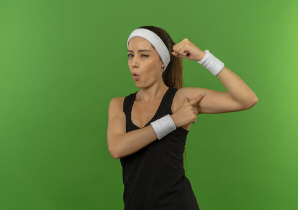 拳身穿运动服的年轻健身女士 头箍扬起拳头 站在绿色的墙壁上 露出自信的二头肌女健身运动装