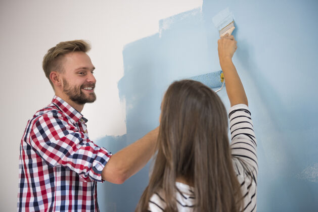搬家一对年轻夫妇在画一堵蓝色的墙迷人的女人室内家居室内
