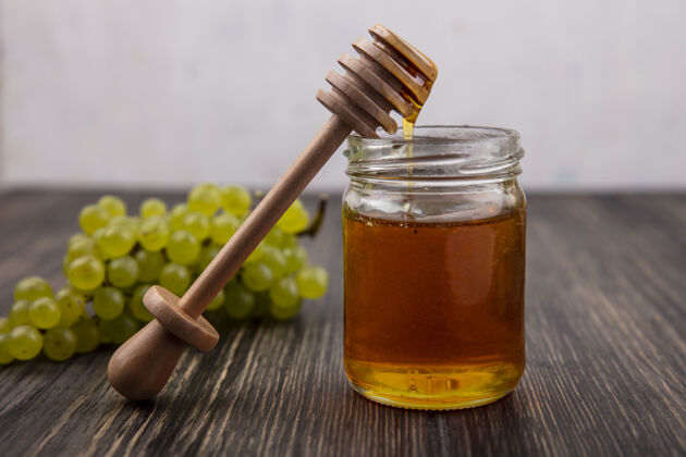 甜味前视图蜂蜜在一个木勺和绿色葡萄罐子和木制背景上蜂蜜罐子食物