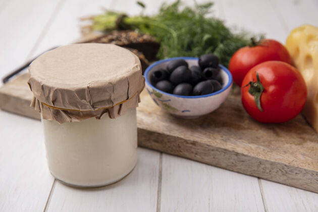 面包前视图酸奶在一个罐子里 橄榄 西红柿 棕色面包和莳萝片放在一个白色背景的架子上白色棕色早餐