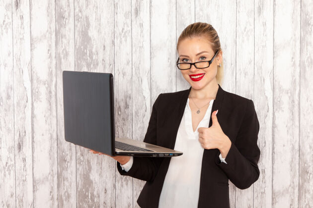 工作正面图：穿着黑色夹克的年轻女商人在白色办公桌上微笑着使用笔记本电脑夹克商务女士严格