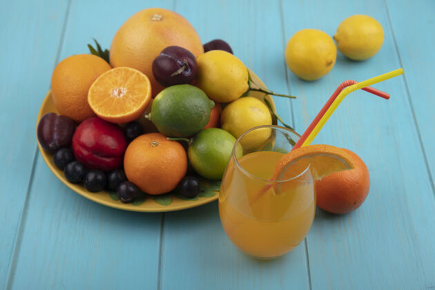 酸橙前视图橙汁在一个玻璃与樱桃李子橙子李子柠檬与酸橙在一个黄色的盘子上的青绿色背景黄色前面风景