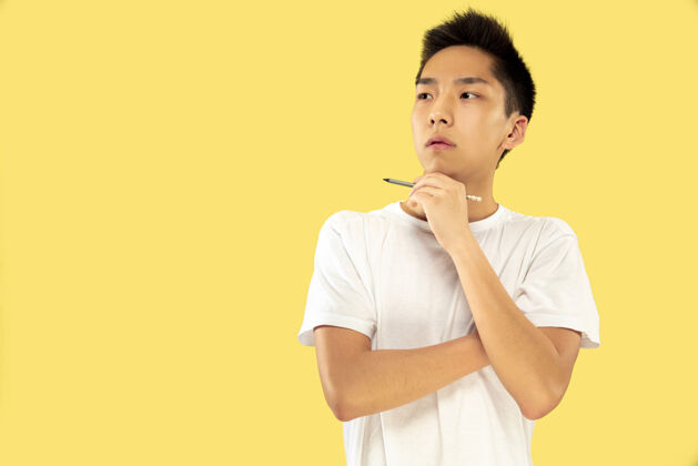 亚洲人黄色摄影棚背景上的韩国年轻人半身像身穿白衬衫的男模站着沉思的薄饼人类情感的概念 面部表情前视图员工英俊人