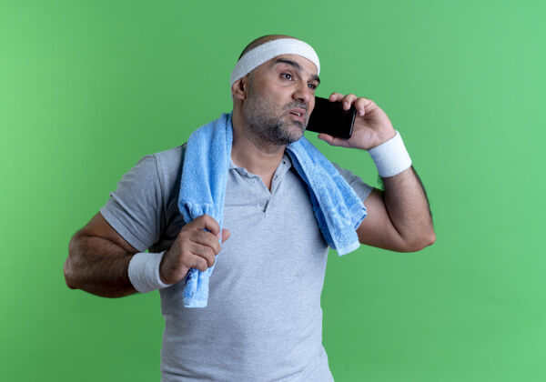 站戴着头巾 脖子上缠着毛巾 站在绿色的墙壁上讲手机 看上去很困惑的成熟运动型男人看毛巾市民