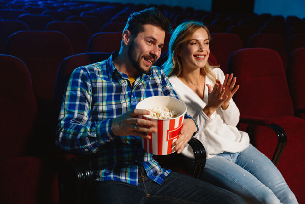 看迷人的年轻白种人夫妇在电影院 房子或电影院看电影看起来富于表现力 惊讶和情绪化独自坐着玩关系 爱情 家庭 周末时间电影院女孩大厅