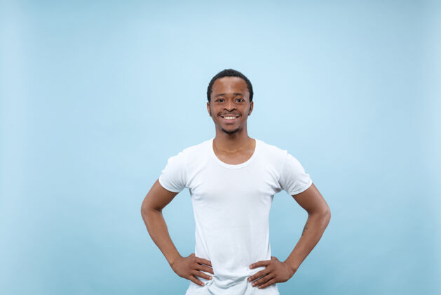 行政人员在蓝色背景上 一位身穿白衬衫的非洲裔美国年轻人的半身特写肖像人类情感 面部表情 广告概念站立和微笑手势胡须看