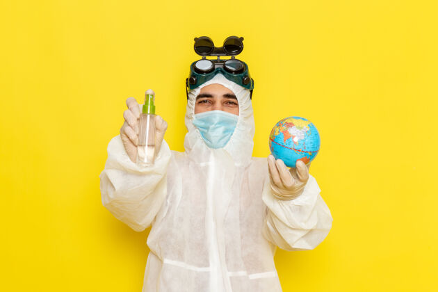 西装正面图男科学工作者穿着特殊的衣服拿着小圆球 喷在黄色的表面化学地球仪封面