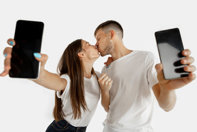 男性这对美丽的年轻夫妇的肖像被隔离在白色的工作室背景上面部表情 人类情感 广告  金融概念男人和女人拿着智能手机和屏幕惊奇肖像微笑