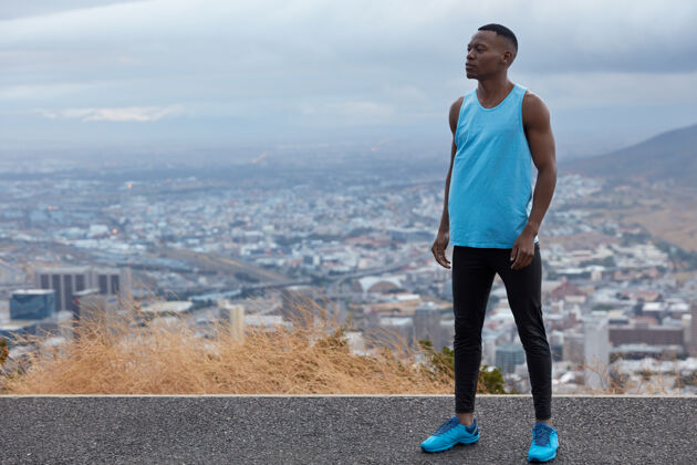 高速公路照片中的黑人运动员穿着蓝色运动鞋 背心和紧身裤 模特们与地平线上的高度 大城市和大山交相辉映 自由空间供您参考全景图运动员户外肌肉
