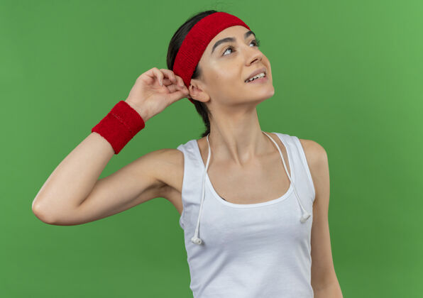 年轻穿着运动服的年轻健身女士 头上戴着头巾 微笑着抬头 感觉积极的情绪抚摸着她站在绿色墙壁上的头巾触摸姿势人