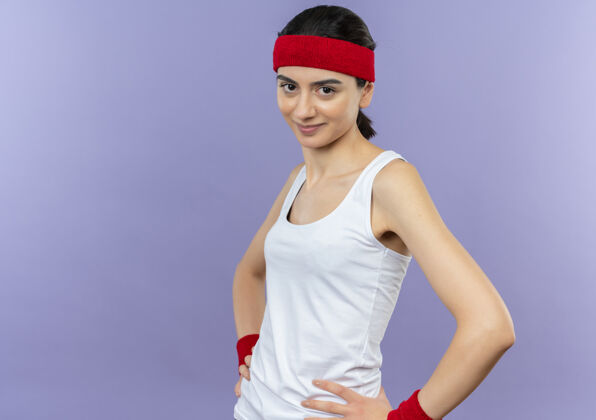市民身穿运动服 头戴头巾 自信微笑的年轻健身女士站在紫色的墙上人姿势运动