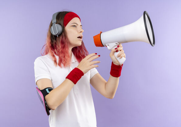 摆姿势年轻的运动型女人站在紫色的墙上对着扩音器大声喊叫运动的女人运动装