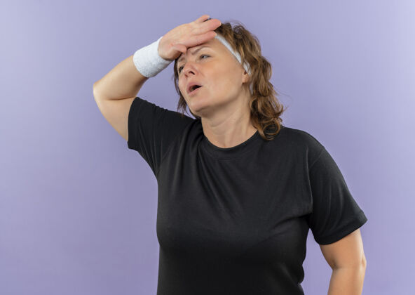 头中年运动女性 身穿黑色t恤 戴着头巾 手放在头上 站在蓝色的墙上 劳累疲惫疲倦锻炼运动装