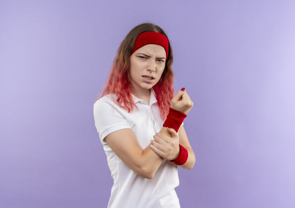 运动年轻的运动型女人站在紫色的墙上 看着不舒服 摸着她的手感到疼痛运动装人不适