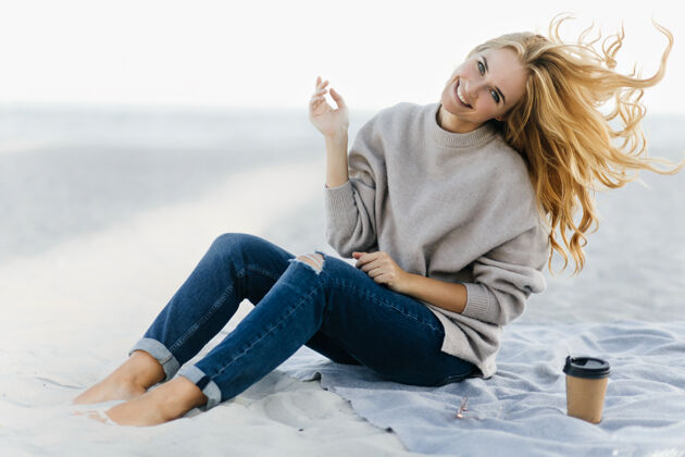风穿着柔软毛衣的积极女人在沙滩上嬉戏迷人的女模特坐在沙滩上喝茶的户外写真自然欢呼女性