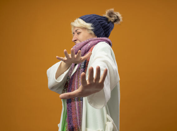 生病生病的不健康的女人 短头发 戴着暖和的围巾和帽子 双手站在橙色背景上做防御手势温暖手使