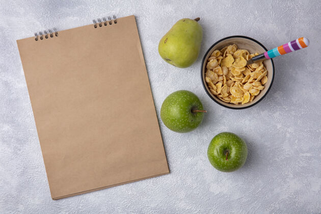 梨顶视图复制空间米色记事本与绿色苹果玉米片在一个碗与勺子和梨在白色背景苹果副本碗