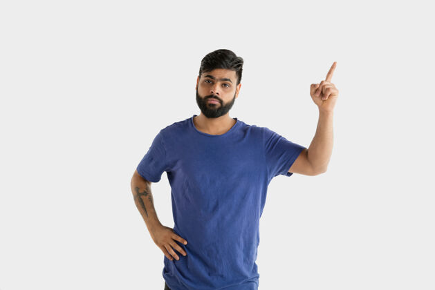胡须美丽的男性半身肖像隔离在白色的工作室背景年轻的情感印度教男子在蓝色衬衫面部表情 人类情感 广告概念指向和选择情绪消极表情