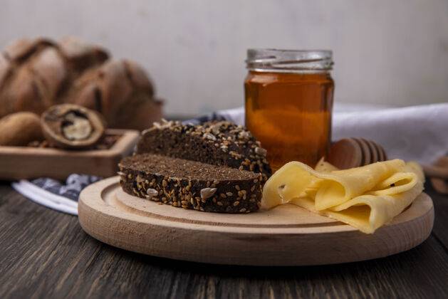 核桃正面图蜂蜜在一个罐子里 黑面包和奶酪放在一个架子上 胡桃木背景风景黑色面包