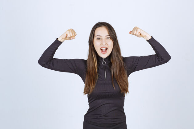 女人穿黑色衣服的女孩露出她的拳头和手臂肌肉年轻自信聪明