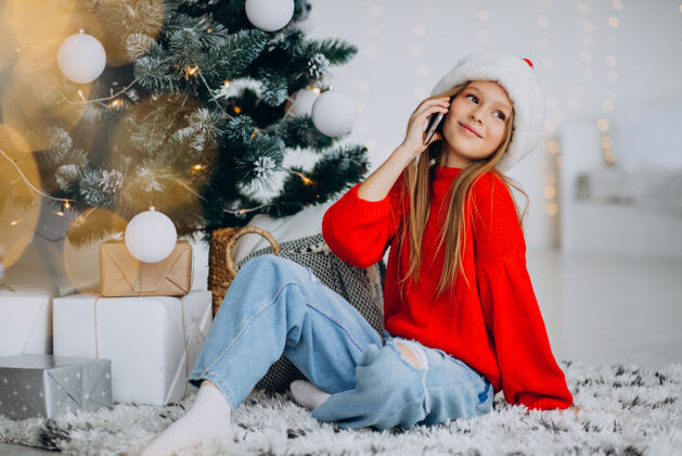 家庭圣诞节 在圣诞树旁打电话的女孩网上商店积极圣诞老人