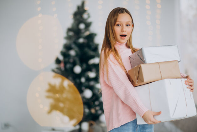 传统可爱的女孩拿着圣诞礼物在圣诞树旁积极看圣诞礼物
