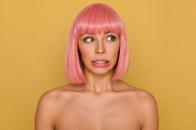 特写困惑的年轻漂亮的蓝眼睛粉红色头发的女性 鲍勃的头发显示她的牙齿 而推尴尬她的嘴 隔离在芥末墙肖像自然前锁