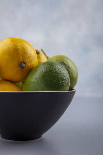 柑橘侧视图在灰色背景上的黑色碗中的酸橙和柠檬酸橙水果黑