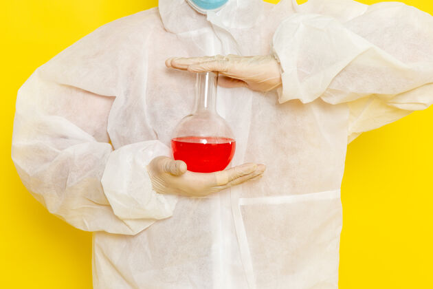 保护正面图穿着特殊防护服的男科学工作者拿着黄色表面上有红色溶液的烧瓶溶液医疗西装