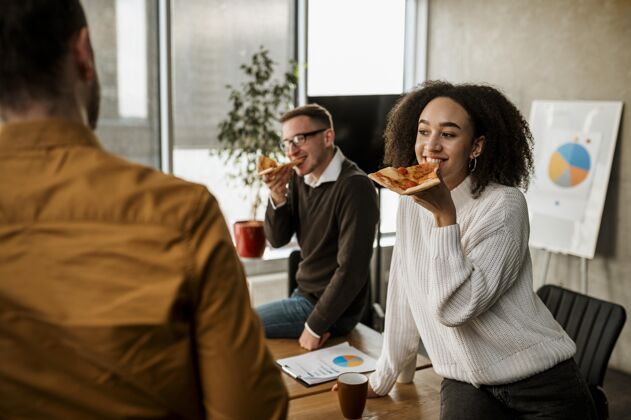 女人笑脸同事在办公室会议休息时吃披萨公司男性工作