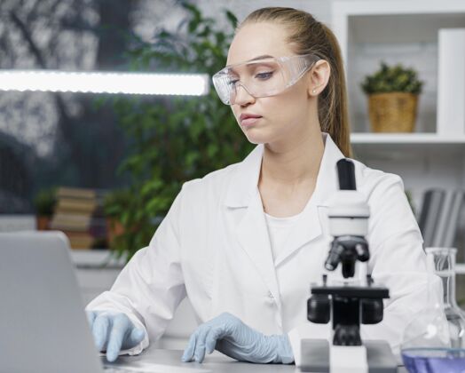 安全眼镜戴着安全眼镜和显微镜的女研究人员在实验室的前视图发明家专家实验室技术人员