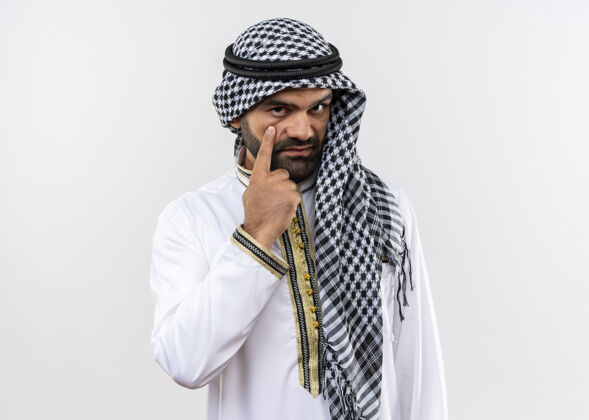 传统一位身着传统服装的阿拉伯男子站在白墙上 用自信的表情指着自己的眼睛站立穿着阿拉伯语