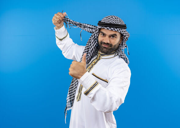 男人身着传统服装的阿拉伯男子微笑着竖起大拇指站在蓝色的墙上站秀传统