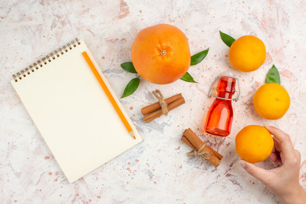 柑橘顶视图新鲜的橘子肉桂棒洋柑在女性手中一支铅笔一本笔记本在明亮的表面柑橘明亮鲜橙