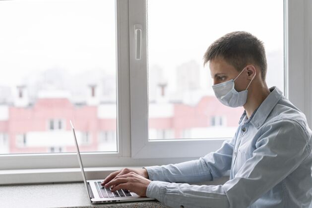 流行病戴着医用面罩的人在笔记本电脑上工作的侧视图安全病毒大流行