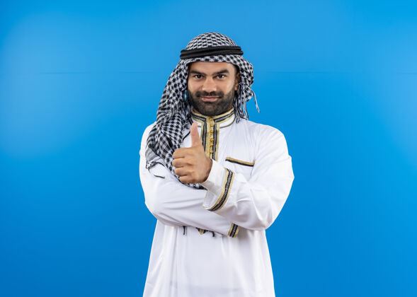 男人身着传统服装的阿拉伯男子 脸上带着微笑 站在蓝色的墙上竖起大拇指秀站传统