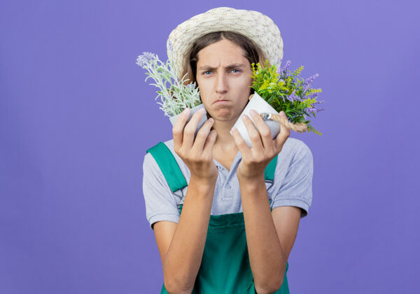 植物年轻的园丁 穿着连体衣 戴着帽子 手里拿着盆栽植物盆栽园丁困惑