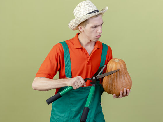 脸年轻的园丁穿着连体衣戴着帽子拿着南瓜剪子年轻帽子