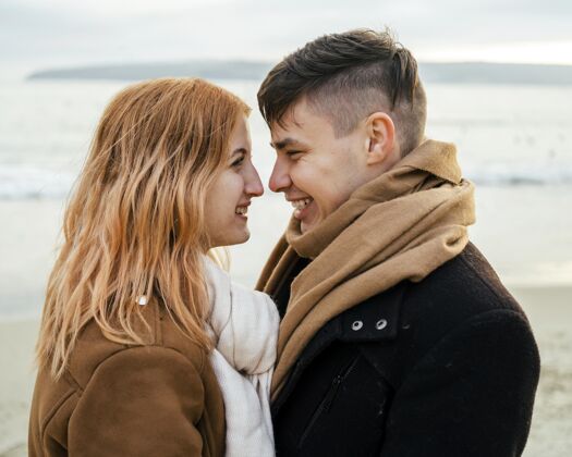 消遣爱微笑的年轻夫妇在冬天的海滩情侣冬天男人