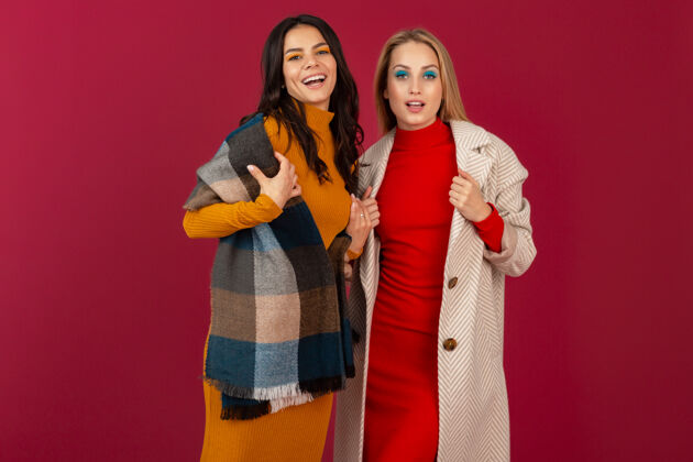 漂亮两位笑容可掬的时尚女性穿着秋冬时装和外套 在红墙上孤零零地摆着姿势套装女性年轻