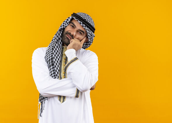 商务人士身着传统服装的阿拉伯商人站在橙色的墙上 面带微笑 看上去既疲惫又无聊看笑无聊