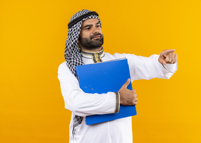 壁板身着传统服装的阿拉伯商人手持蓝色文件夹 一边看一边用手指指着站在橙色墙上的一边旁边文件夹拿着
