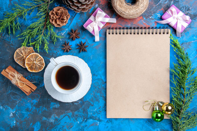 扣子俯瞰笔记本上的圣诞球松树枝桂枝八角干柠檬片一杯茶在蓝色的表面顶咖啡茴香