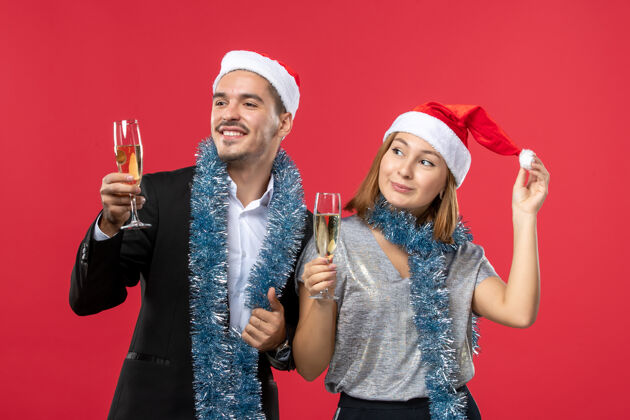 年轻夫妇正面图年轻夫妇在红墙庆祝新年爱圣诞派对饮料微笑风景帽子