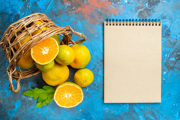 篮子俯瞰柳条篮子上的新鲜柑橘蓝色表面上的笔记本维生素笔记本顶部