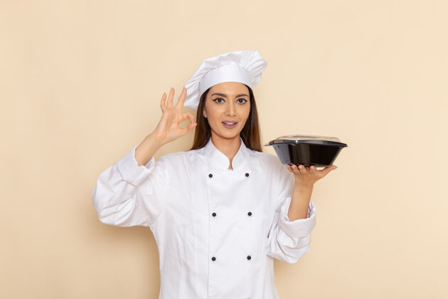 年轻身穿白色厨师服的年轻女厨师正拿着黑色碗站在浅白的墙上工作烹饪套装